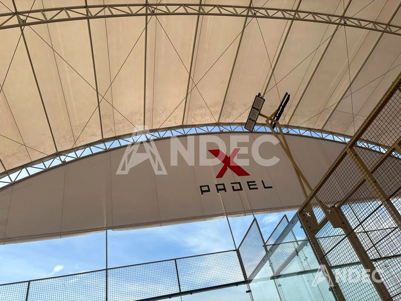Detalle del cierre frontal en lona PVC y de la cobertura curva del complejo deportivo, con la iluminación instalada