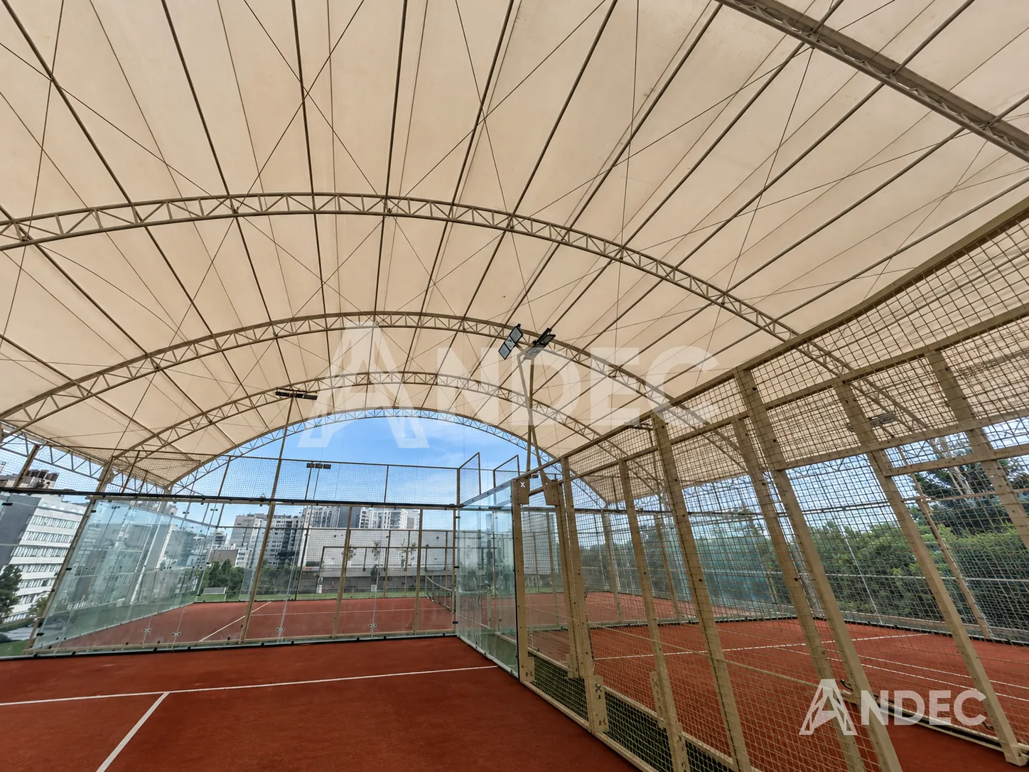Estructura metálica curva con tijerales y cobertura de lona PVC tensada, vista desde la cancha