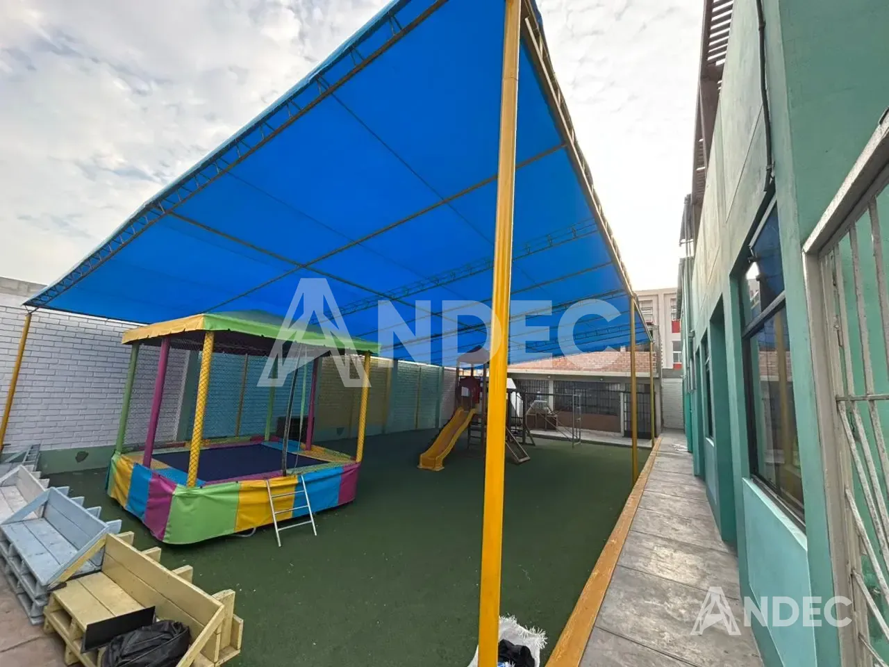 Cobertura de lona PVC azul sobre estructura metálica amarilla en el patio del colegio Rosa Maura