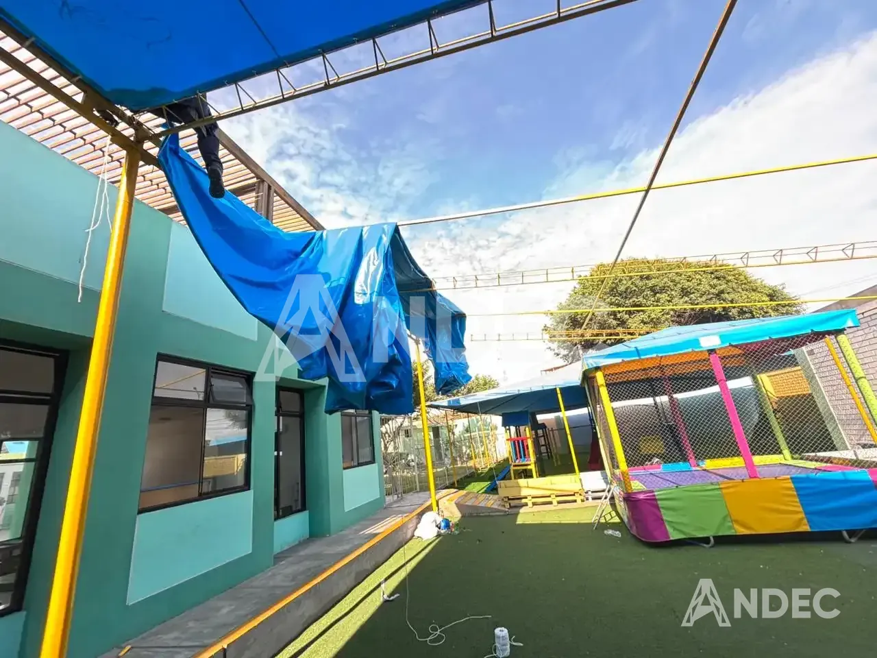 Inicio del montaje de la cobertura de lona PVC azul sobre el patio del colegio, con la lona aún plegada en la estructura