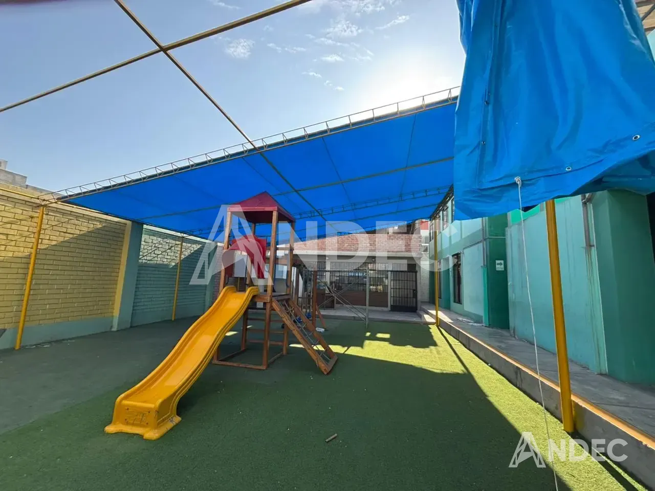 Patio de juegos del colegio con tobogán bajo la cobertura de lona PVC azul