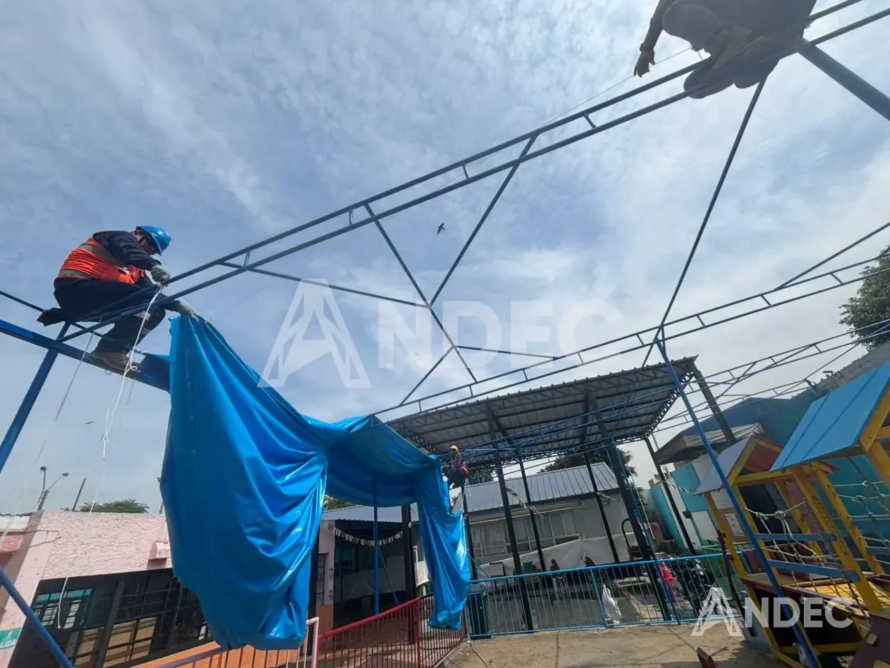 Operario de ANDEC subiendo la lona PVC azul a la estructura durante el montaje