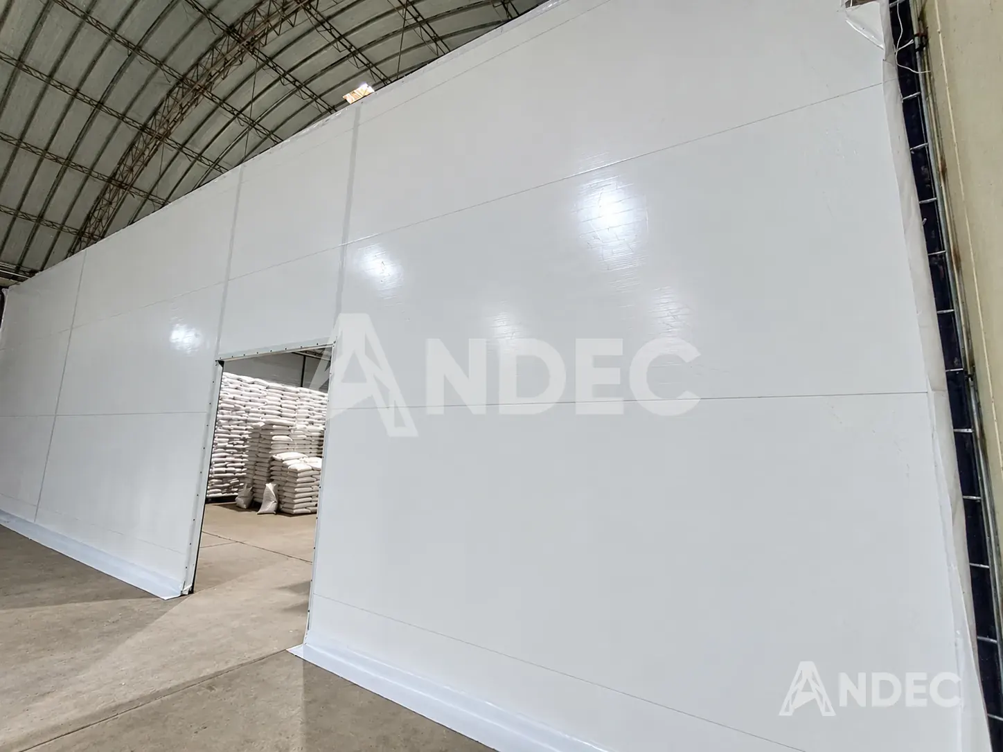 Puerta de acceso en la pared de lona PVC blanca, con sacos de grano apilados al fondo