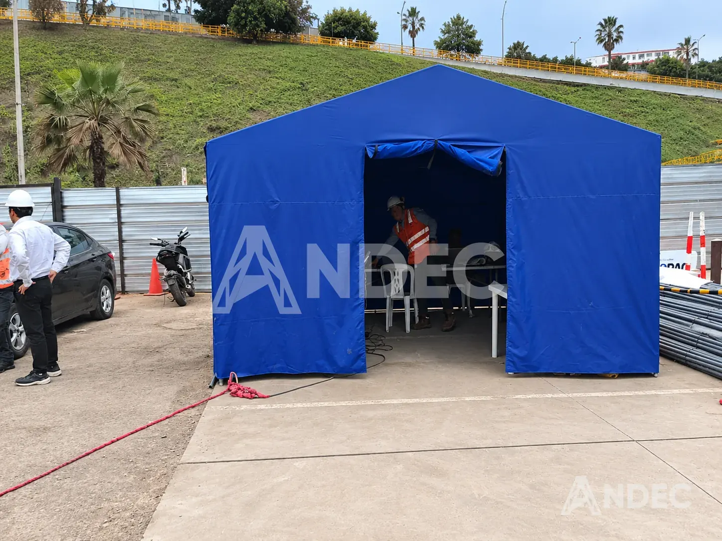Carpa dos aguas azul en uso como oficina de obra, con personal en el interior