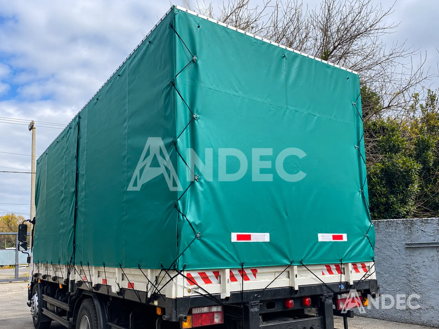 Toldera de lona PVC verde amarrada con soga perimetral por los ojales sobre la carrocería de un camión