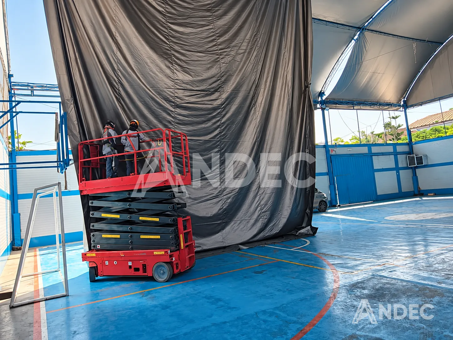 Instalación de una cortina de lona PVC BlackOut negra con elevador de tijera en una losa deportiva