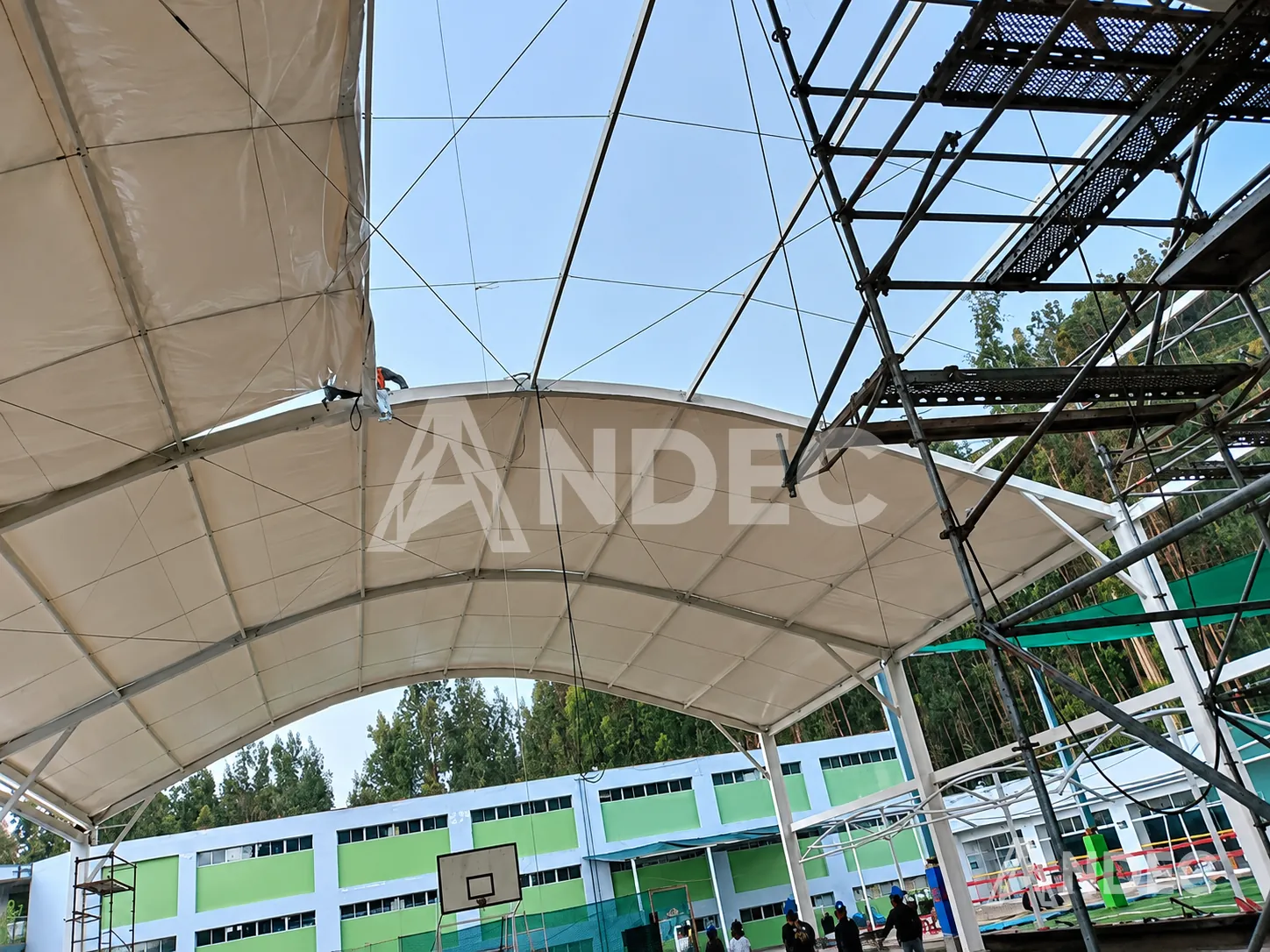 Cobertura curva en lona PVC blanca tensada sobre estructura metálica en una losa deportiva escolar